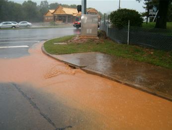 Photo of sediment-laden runoff flowing into a catch basin on a street corner 